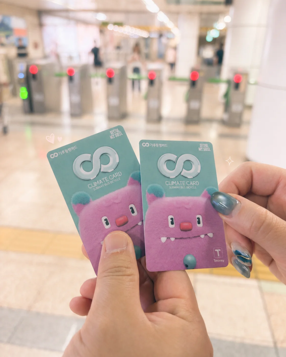 Two pink monster-character Climate Cards, held up at a Seoul subway station gate