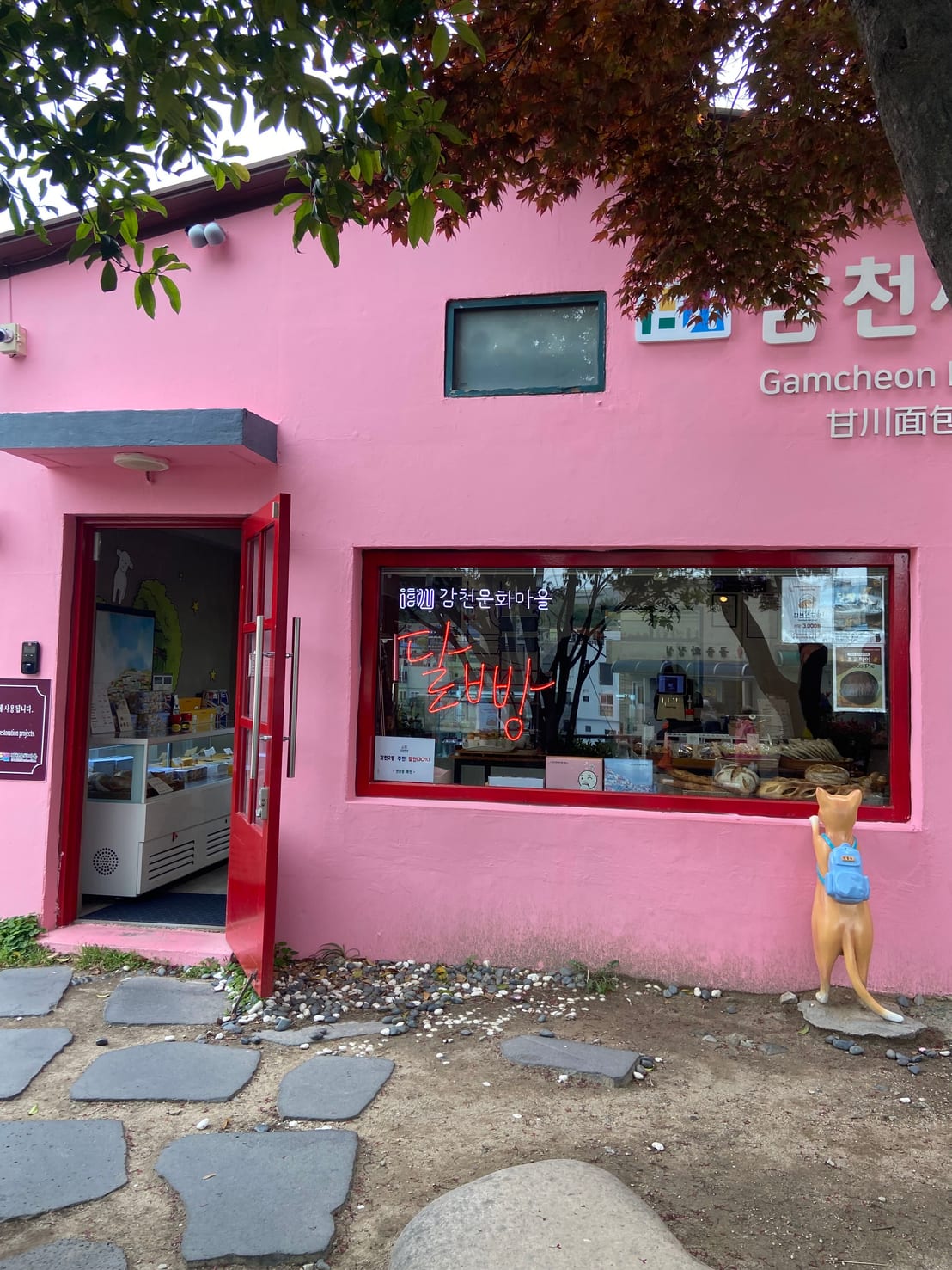 A pink Gamcheon bakery storefront with a neon sign and a fox statue out front