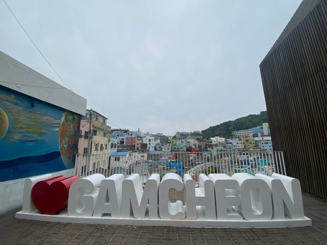 An 'I ❤ GAMCHEON' sculpture at a viewpoint overlooking the colorful hillside houses of Gamcheon Culture Village