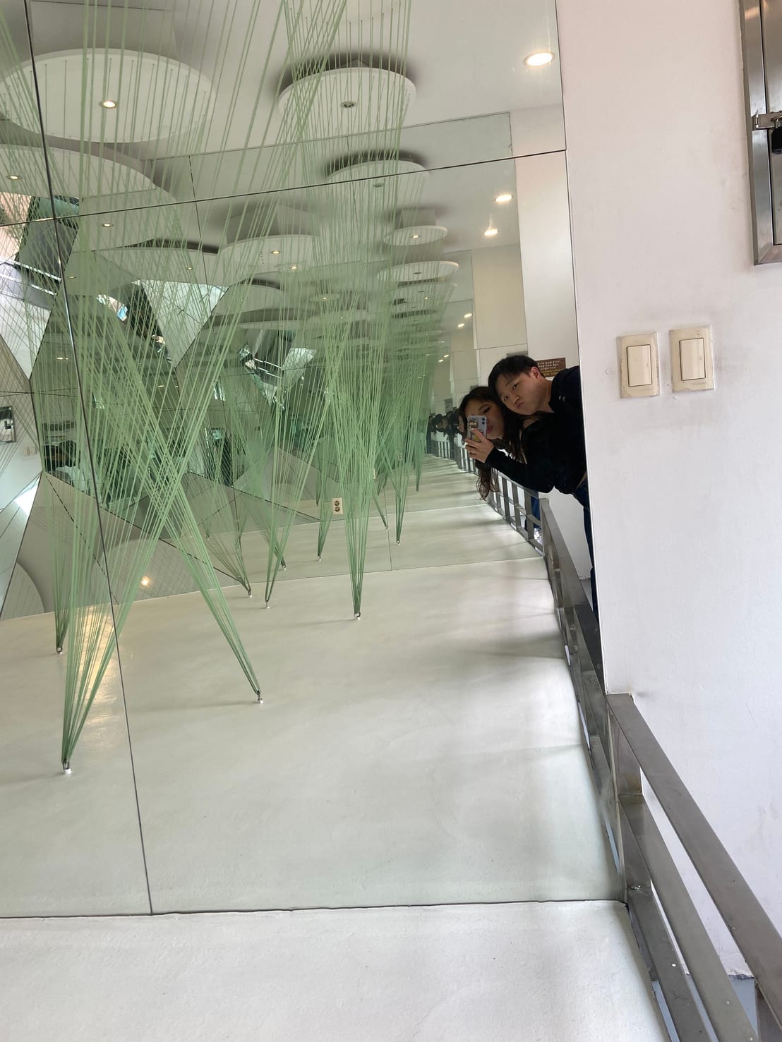 A mirrored corridor art installation with green string sculptures hanging from the ceiling
