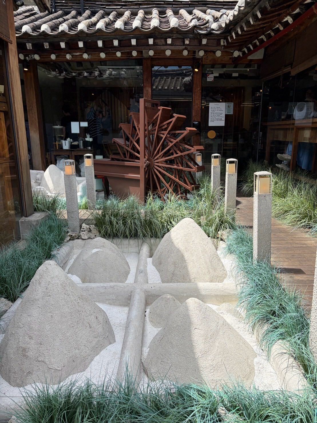 A traditional wooden waterwheel and millstones in a cafe's hanok courtyard entrance