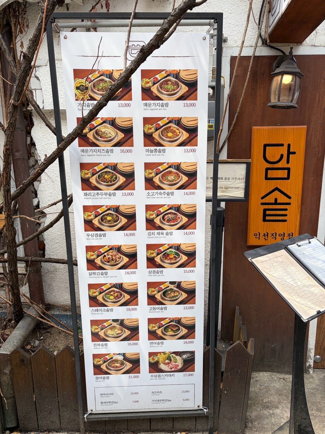The Damsot Ikseon-dong menu board listing pot rice varieties and prices, next to the restaurant's wooden signage