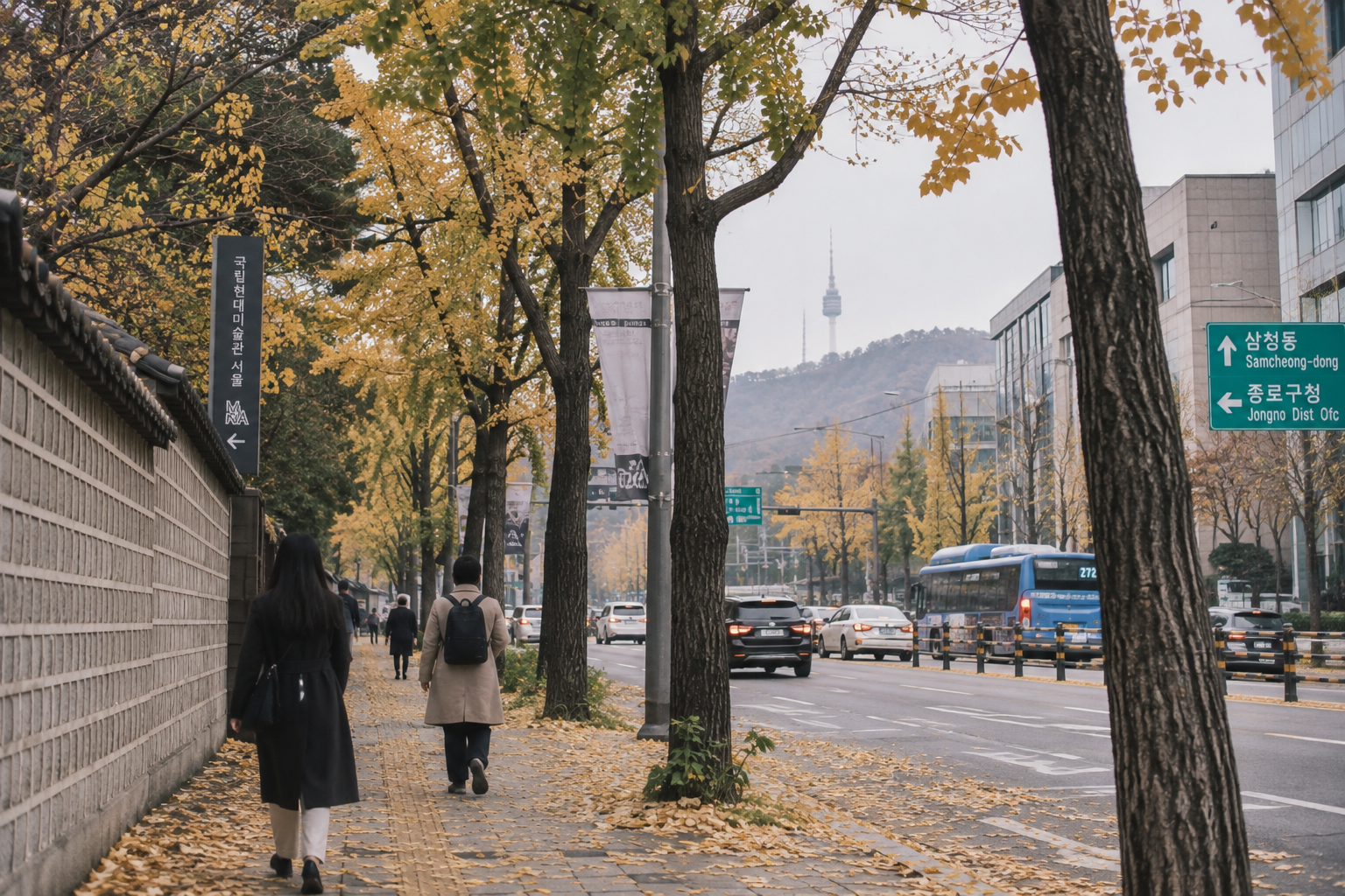 A Seoul street lined with golden ginkgo trees, N Seoul Tower visible on the hill behind, pedestrians walking underneath
