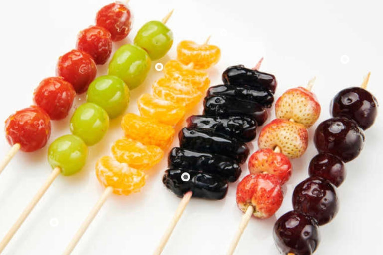 Rows of tanghulu fruit skewers — candied cherry tomatoes, grapes, mandarin segments, dates, strawberries, and more, each coated in a glossy hard candy shell