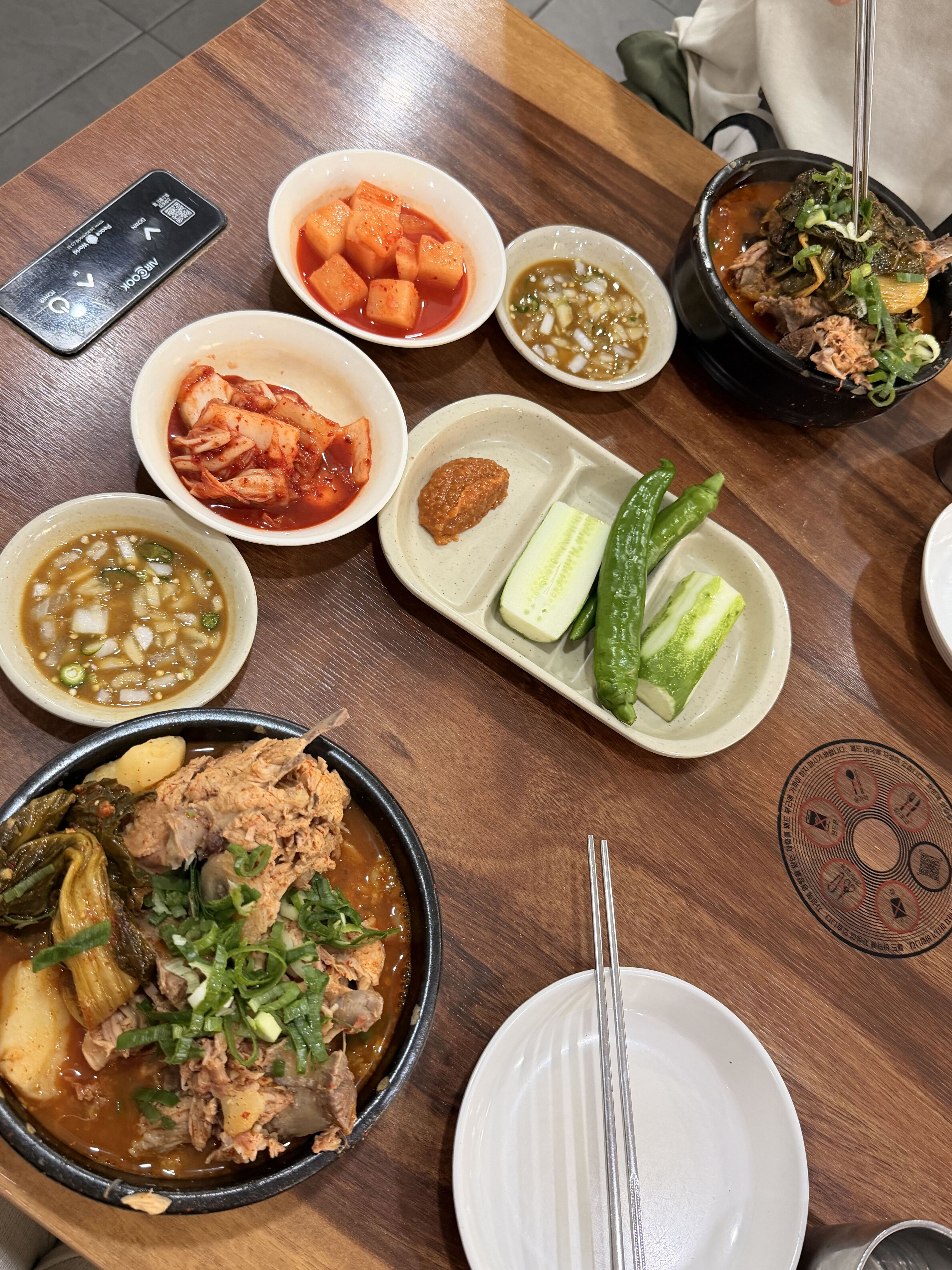 A large bowl of Korean gamjatang spicy pork-bone soup with potatoes and greens, served with side dishes