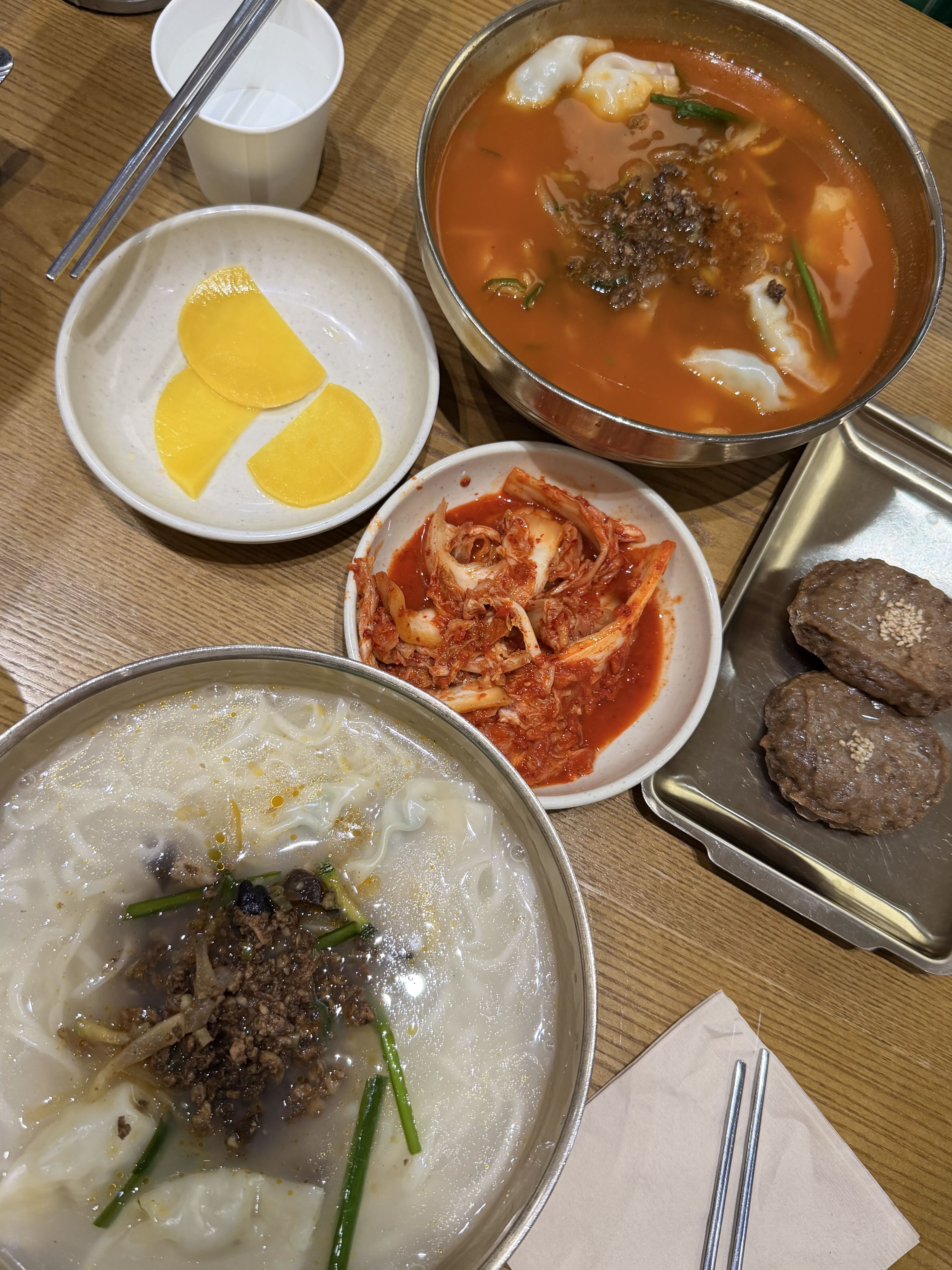 A bowl of Korean kalguksu with hand-cut noodles in a creamy white broth, served with kimchi and dumplings