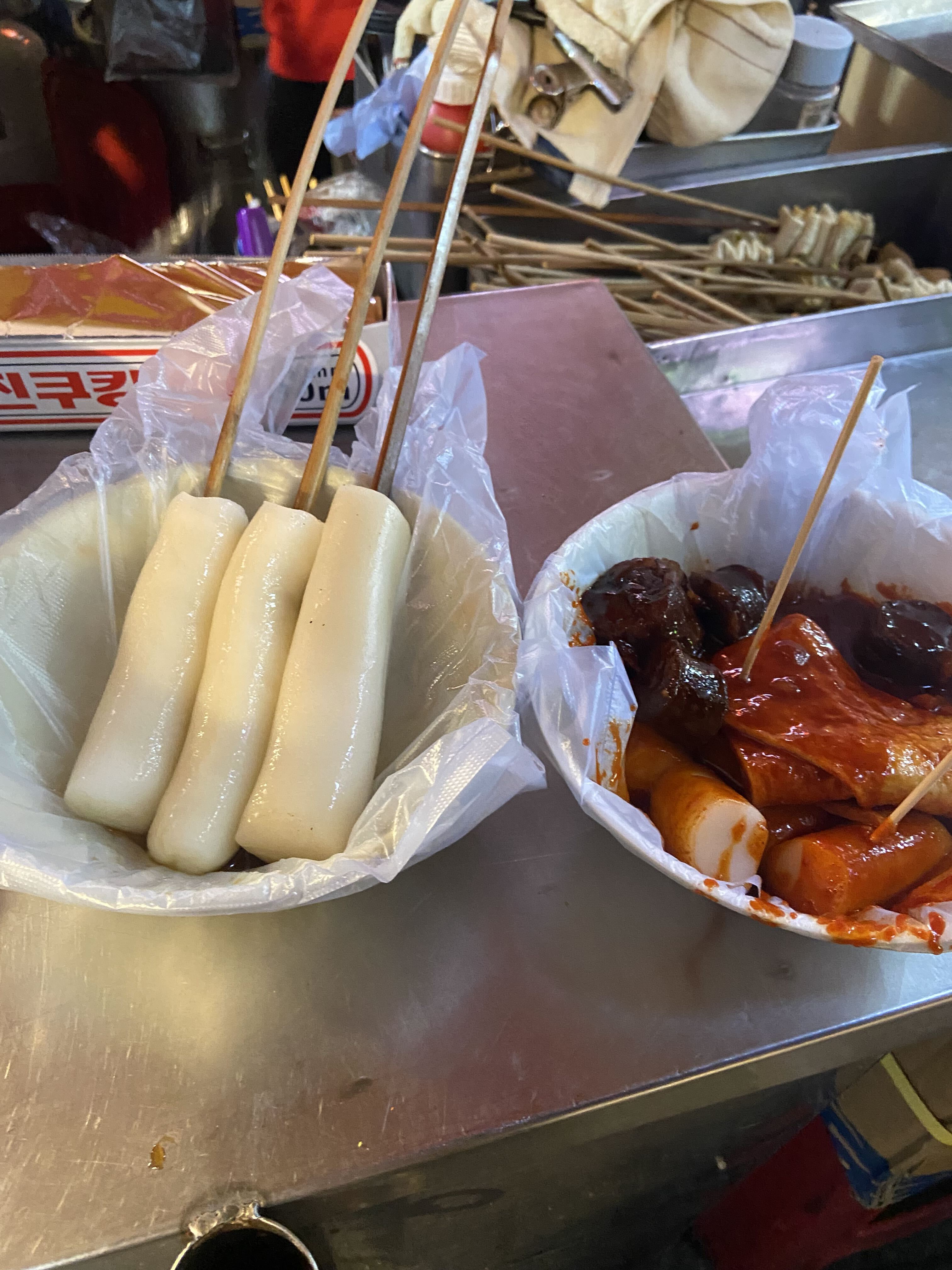 Fresh rice cakes and sauce-coated tteokbokki on skewers at a Korean street-food stall