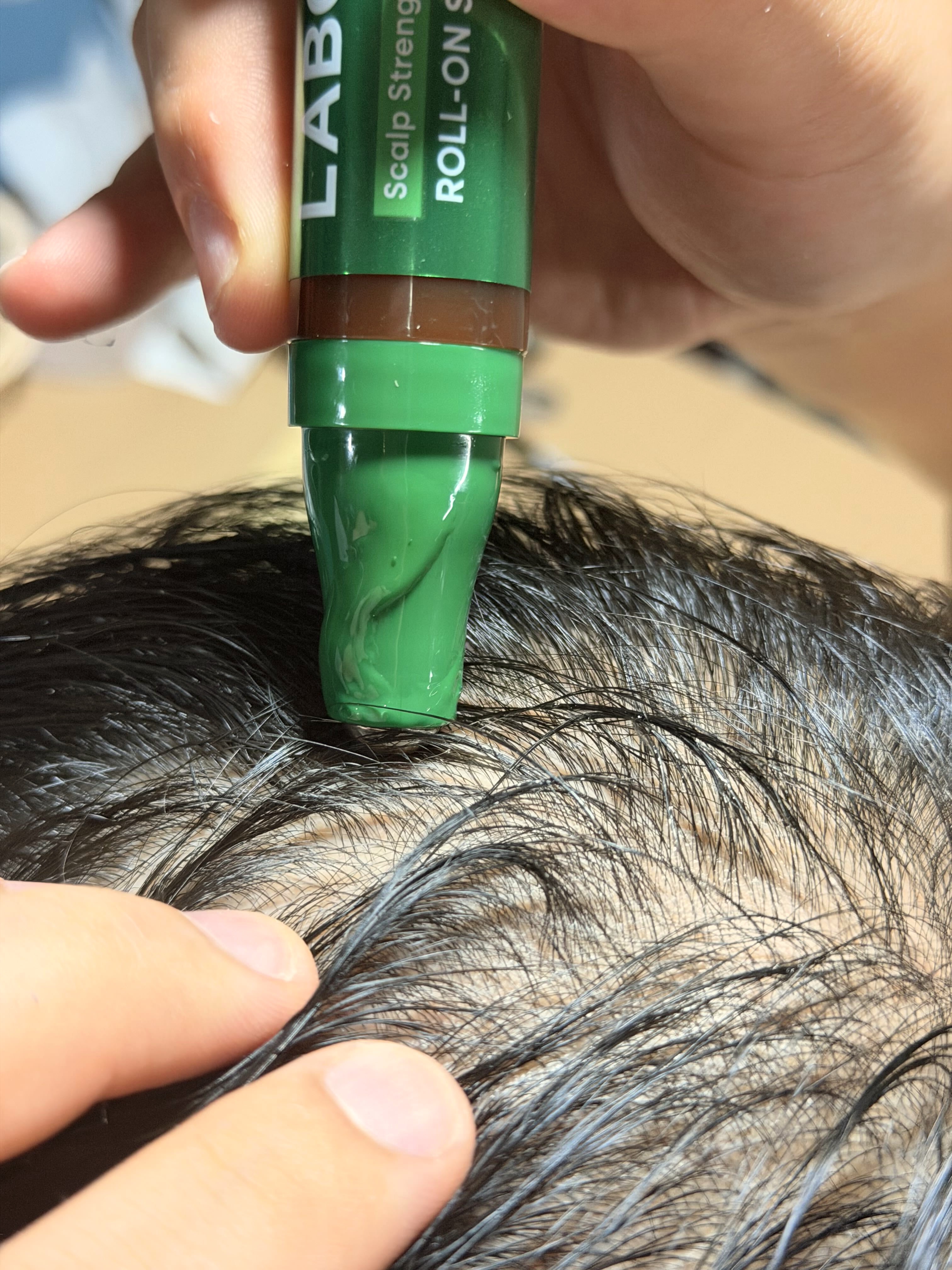 The LABO·H roll-on serum being applied directly to a scalp, parting the hair with a finger