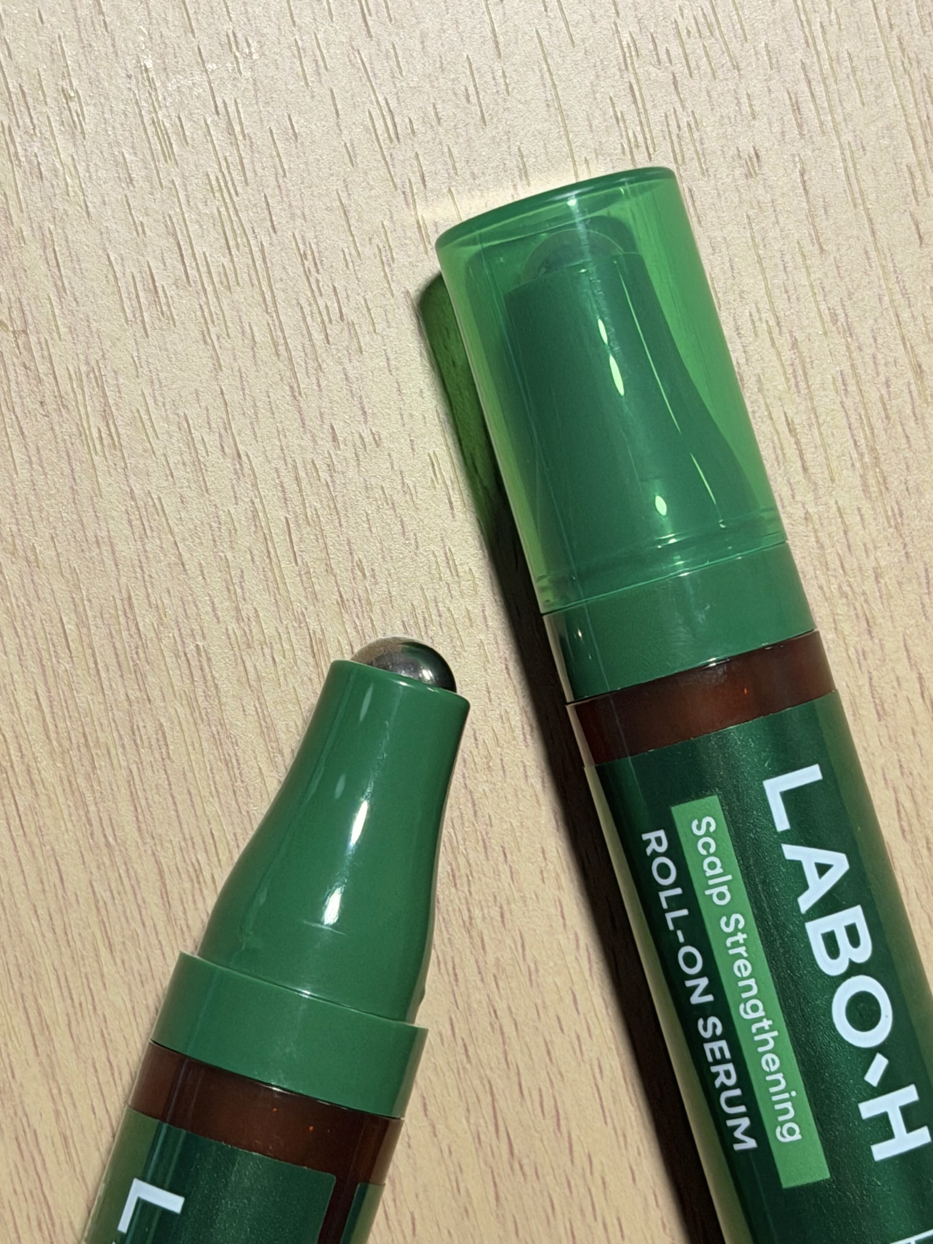 A hand holding the LABO·H roll-on serum, showing the rollerball tip up close