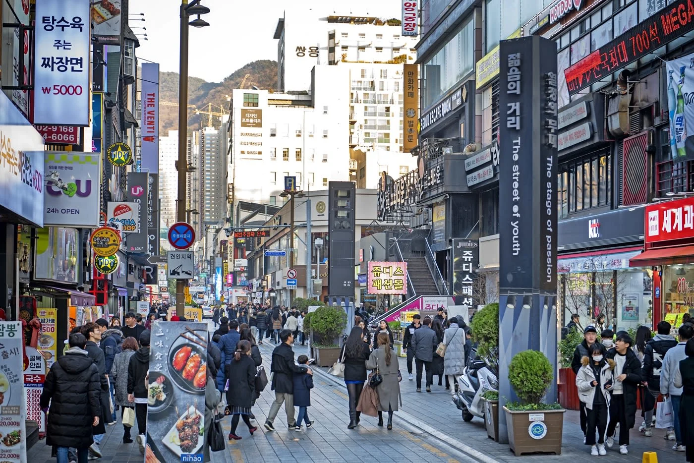 A crowded pedestrian shopping street in Seomyeon, Busan, lined with storefronts and neon signs