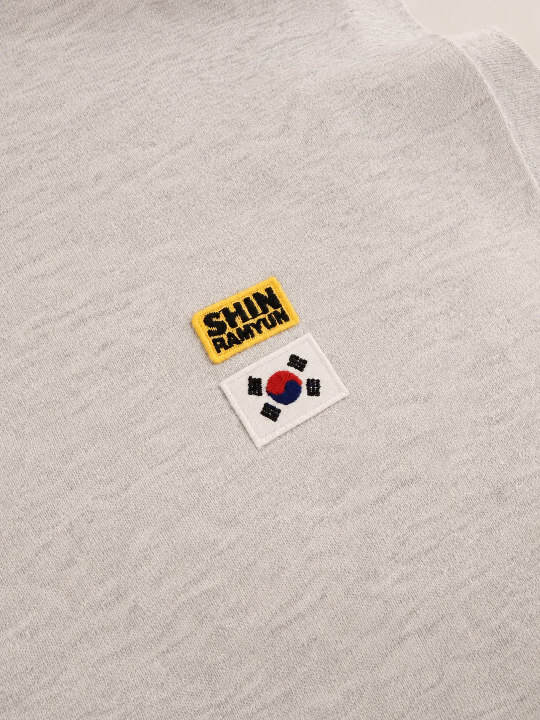 Close-up of the SHIN RAMYUN patch and Korean flag patch heat-pressed onto the grey T-shirt