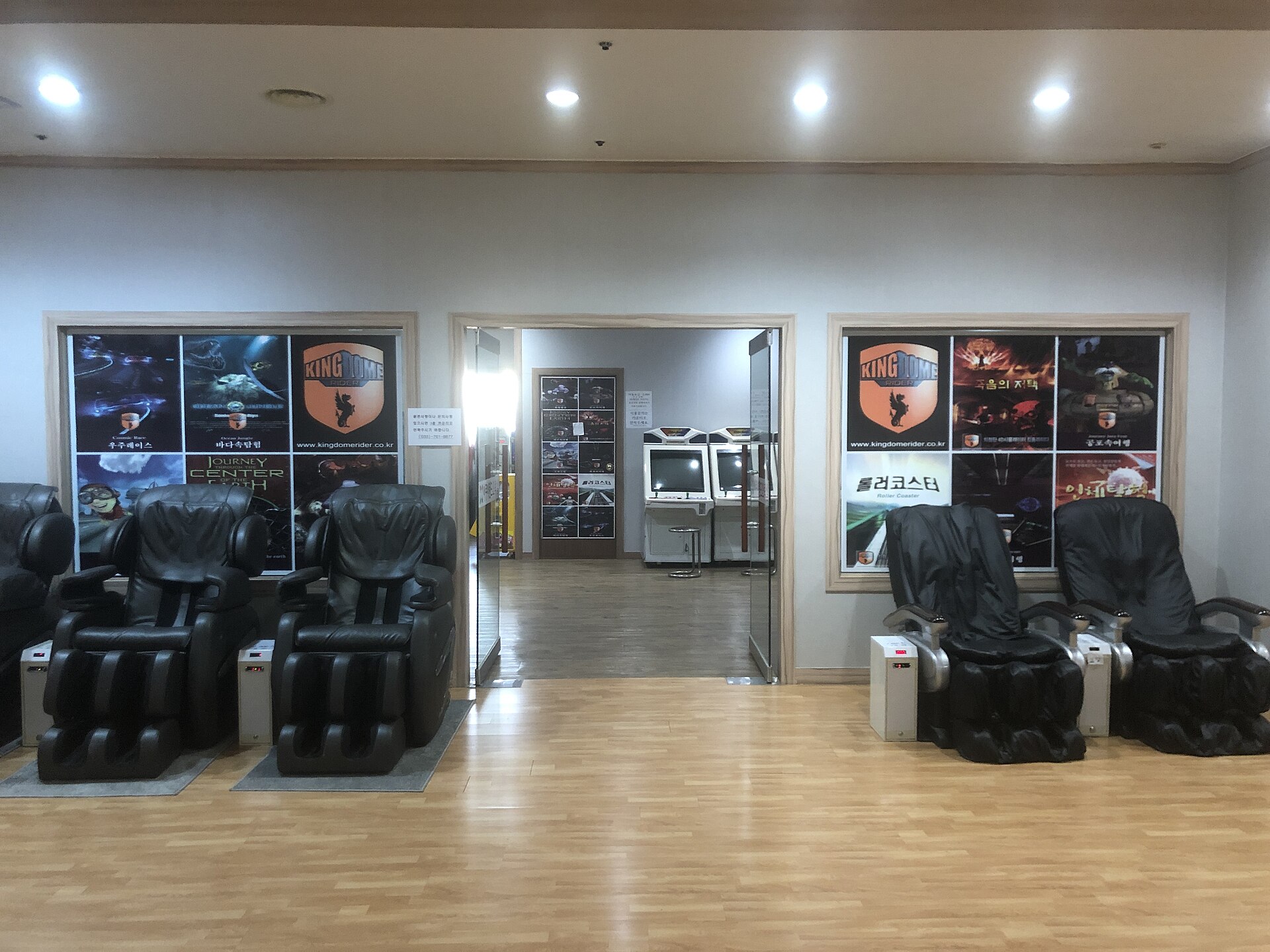 A row of black leather massage chairs in a jjimjilbang lounge with a wooden floor