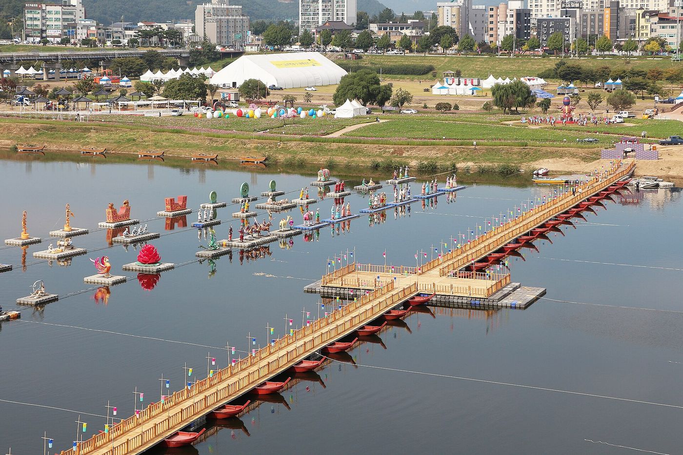 Rows of colorful lantern floats and a pontoon footbridge on the Geum River in Gongju, with festival tents on the riverbank