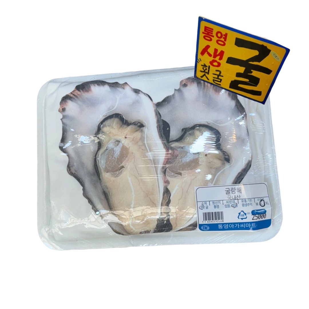 A T-shirt printed with two giant oysters, shrink-wrapped on a white foam seafood tray with a yellow '통영 생굴' price card and a 굴랑해 label
